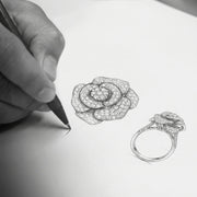 A hand drawing a rose-shaped diamond ring in pencil
